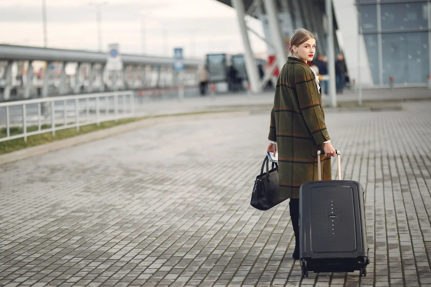 A traveller walking away from an airport terminal with a suitcase, heading for the rental pickup