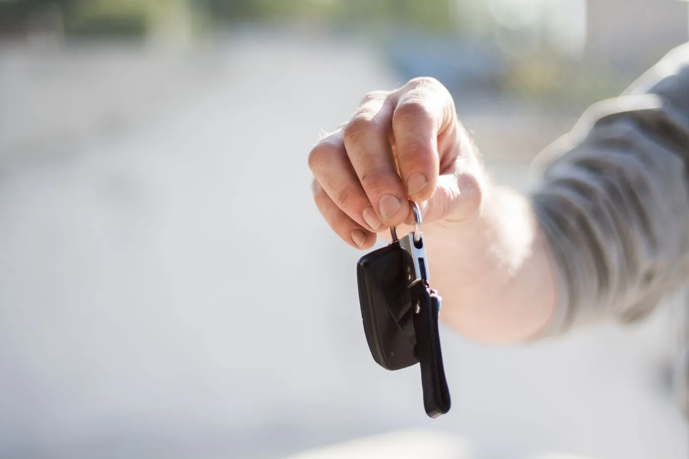 A hand holding out a car key on its ring, ready to hand over to a renter