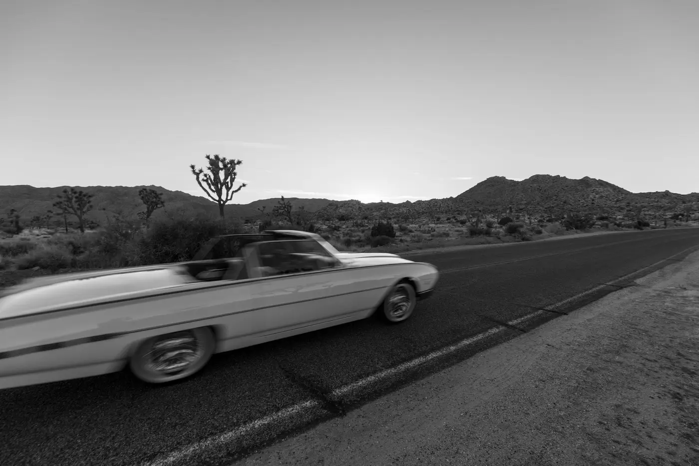 A convertible on an open desert highway at dusk, part way through a one way trip
