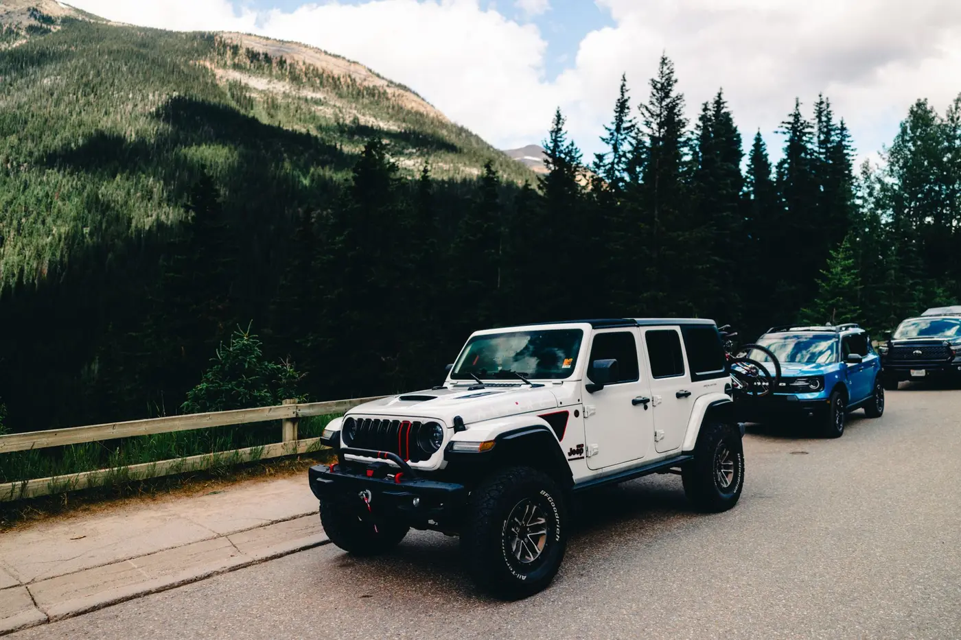 An SUV parked on a forest road with mountains behind it