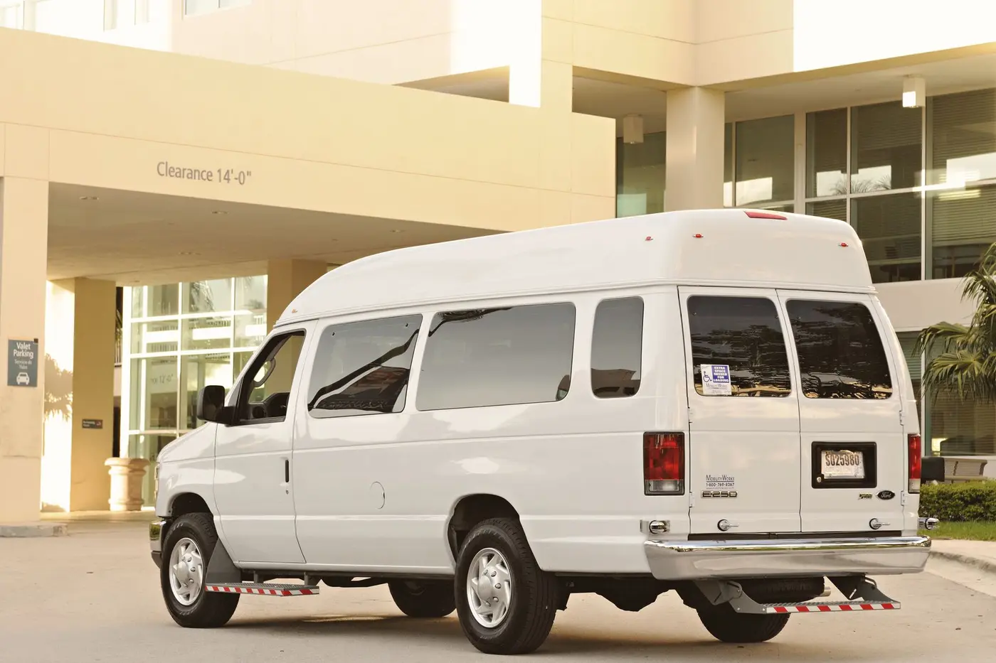 A white high-roof passenger van parked at the entrance of an office building